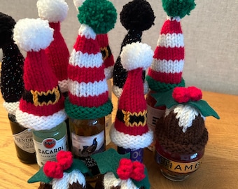 May include: A collection of miniature knitted bottle toppers including red and white striped Santa hats with green pom-poms, solid red Santa hats with white pom-poms, black hats, and brown Christmas pudding toppers with green felt holly leaves.