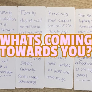 May include: A set of white cards with handwritten text, featuring phrases such as "Incoming Reconciliation" and "Family drama." A banner across the cards reads "WHAT'S COMING TOWARDS YOU?"
