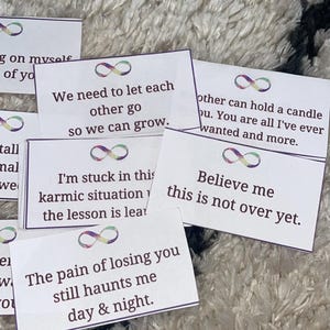 May include: A collection of white cards with purple borders and infinity symbols, each bearing a different message in black text. The cards are arranged on a white, textured surface, with phrases like "We need to let each other go."