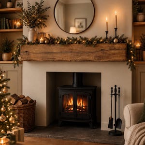 May include: A black wood-burning stove sits inside a fireplace with a thick, rustic wooden mantel. The mantel is decorated with a green pine garland, string lights, two tall taper candles in black holders, and a round mirror hanging above.