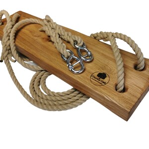May include: A wooden swing set with two rope loops and metal hooks. The swing is made of natural wood and has a brown finish. The rope is natural colored and is tied to the swing with metal hooks. The swing is labeled "Charley Oak" in the center.