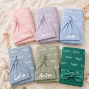 May include: Six sets of baby blankets and matching hats in pink, lavender, light blue, dusty blue, sage green, and dark green. Each item features a repeating name pattern and a single large name printed on the front, including Bella, Charlie, Liam, Quinn, Amber, and Violet.
