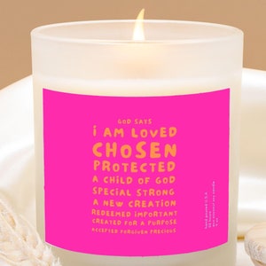 Puede incluir: Una vela de vidrio esmerilado con una etiqueta rosa que dice "GOD SAYS I AM LOVED CHOSEN PROTECTED A CHILD OF GOD SPECIAL STRONG A NEW CREATION REDEEMED IMPORTANT CREATED FOR A PURPOSE ACCEPTED FORGIVEN PRECIOUS".