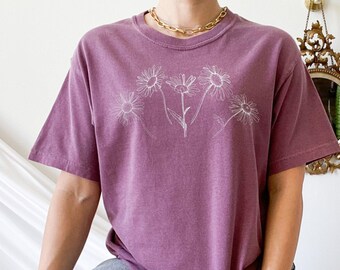 May include: A mauve coloured t-shirt with a white outline of five daisies on the front.