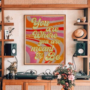 May include: A retro-style poster with a colourful, wavy background. The text on the poster reads "You are where you are meant to be".