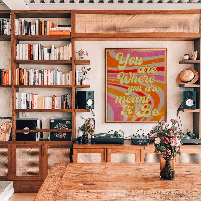 May include: A retro-style poster with a pink, orange and yellow wavy background. The text on the poster reads "You are where you are meant to be".