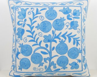 May include: Square throw pillow with a white background and a blue embroidered floral design. The design features stylized flowers and pomegranates. The pillow is a decorative home accent.