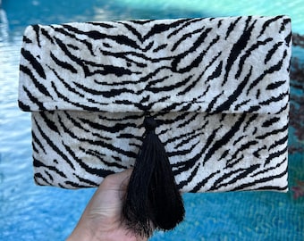 Puede incluir: Un bolso de mano blanco y negro con estampado de cebra y un borla negra.