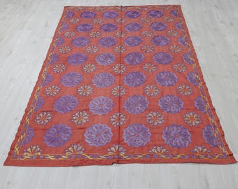 Könnte beinhalten: Ein großes, rechteckiges, rotes Textil mit einem sich wiederholenden Muster aus lila Blumendesigns. Kleinere gelbe und lila Blumenmuster sind dazwischen eingestreut. Die Ränder sind mit einem gelb-violetten Design eingefasst.