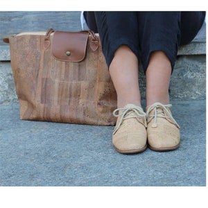 May include: A cork tote bag with a brown leather flap and a cork satchel with brown laces.