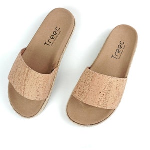 May include: A pair of cork sandals with a brown leather strap and a jute sole. The sandals have the text "Treec from nature to you" printed on the insole.