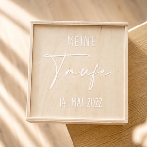 Könnte beinhalten: Eine hellfarbene Holzkiste mit Deckel. Auf dem Deckel stehen die Worte "MEINE Taufe" und "14. MAI 2022" in weißer Schrift. Die Kiste steht auf einer hellfarbenen Holzoberfläche.