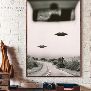 May include: A black and white photograph of a road with three flying saucers in the sky. The road is winding and there is a figure standing in the distance. The image is grainy and has a vintage feel.