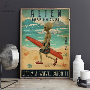 May include: A vintage-style poster with a green alien surfing on a red surfboard. The poster has the text "Alien Surfing Club Est. 1969" and the words "Life's a wave. Catch it." at the bottom.