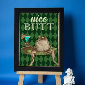 May include: A framed print with a green and white diamond pattern background. A cartoon frog sits on a lily pad holding a blue cocktail. The text "nice BUTT" is printed in white on the print.