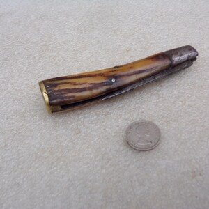 May include: A vintage pocket knife with a brown and white bone handle and a brass bolster. The blade is closed and the knife is in good condition.