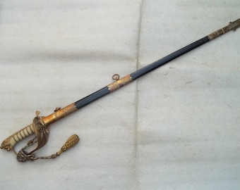 May include: An antique sword with a black blade and ornate gold and ivory hilt. The sword features intricate detailing on the handle and guard, with a decorative tassel attached. The scabbard is black with gold accents.