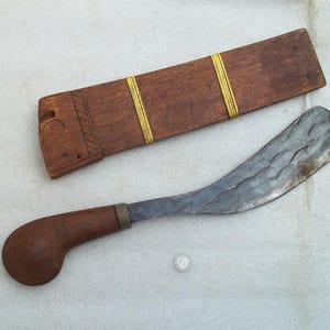 Op de afbeelding: Een gebogen, donkergrijs metalen blad met een houten handvat en een houten schede met gele accenten. De schede heeft een gesneden ontwerp.