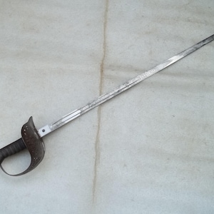May include: An antique sword with a curved handguard and a long, pointed blade. The handle is dark, and the blade shows signs of age and wear. The sword is set against a neutral background, highlighting its historical design.