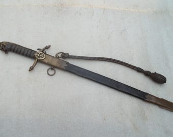 May include: An antique sword with a dark blade and an ornate handle. The hilt features a lion's head and a gold-coloured emblem. A decorative cord and sheath complete the design. The sword is likely a collectible or historical item.