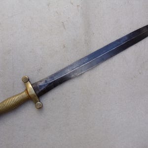 Könnte beinhalten: Ein schwarzes Metallsäbel mit einem Messinggriff und einem dekorativen Spiralmuster. Das Säbel hat eine spitze Spitze und eine gerade Klinge.