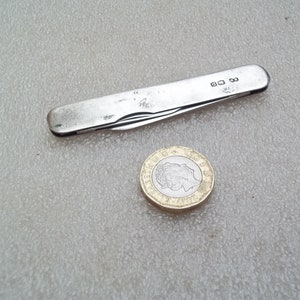 May include: A silver pocket knife with a blade and a small handle. The knife is closed and has a silver hallmark on the handle.