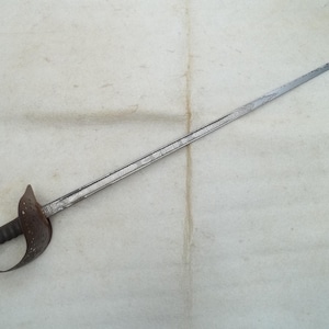May include: A vintage sword with a long, slender, silver blade and a detailed, ornate handle. The handle is dark brown with a curved handguard. The sword is set against a neutral background.