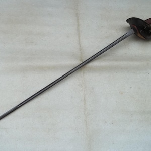 May include: A dark metal sabre with a brown handle and a curved guard. The blade is long and slender, tapering to a sharp point. The hilt features a brown grip and a protective guard. The sword is set against a neutral background.