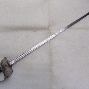 May include: A silver sword with a decorative hilt and a long, straight blade. The sword is lying on a white surface.