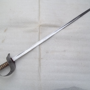 May include: A silver sword with a wooden handle and a decorative guard. The sword is lying on a white surface.