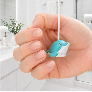 May include: A turquoise and white dolphin-shaped light pull with a white cord. The dolphin has a small, clear gem on its forehead. The light pull is designed for a bathroom setting.