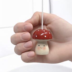 以下が含まれることがあります： 赤い帽子に白い水玉模様、笑顔の顔をしたキノコの形をしたライトプル。白いコードで吊り下げられています。子供部屋やバスルームに最適な、可愛らしいアクセサリーです。
