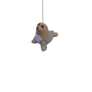 May include: A light brown ceramic seal with a white belly and black eyes. The seal is hanging from a white string.