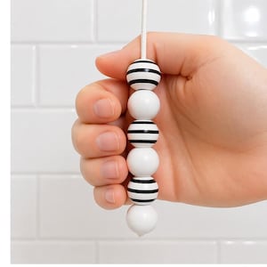 Puxador de luz de madeira com contas listradas em preto e branco, com cordão e conector.