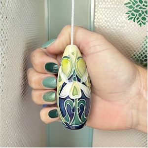 May include: A ceramic light pull with a white flower design on a blue and green background.