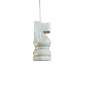 May include: A white ceramic chess knight figurine hanging from a string. The knight is in a classic style with a horse's head and a raised leg.