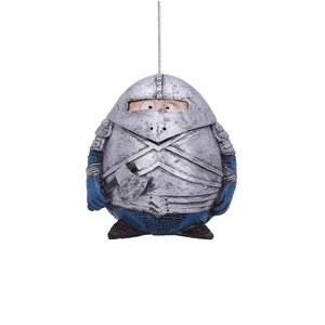 May include: A silver knight figurine in the shape of an egg with blue accents. The knight is wearing a helmet and armor and is holding a sword.