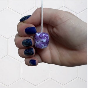 Puede incluir: Una mano sosteniendo un tirador de luz de vidrio morado y blanco con un cordón blanco.