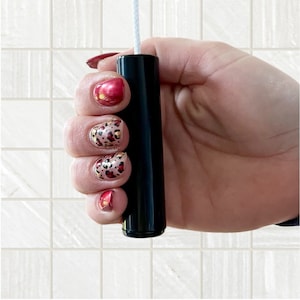 May include: A black cylindrical pull cord for a light fitting. The cord is held in a hand with red and leopard print nail polish.
