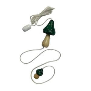 May include: A white cord with two green mushroom-shaped pull cords. The mushrooms have white polka dots.