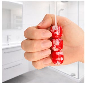 May include: A red and white decorative pull chain for a bathroom light fixture. The pull chain features three red, square beads with white floral patterns. The beads are strung on a white cord.