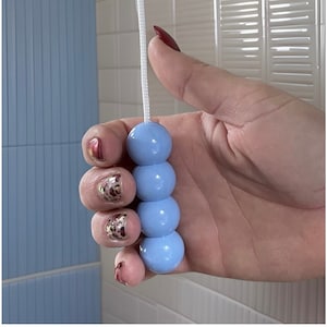 May include: A light blue beaded pull chain for a light fixture or ceiling fan. The pull chain has four round beads and a white cord. The background features blue and white tiles.