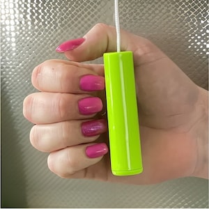 May include: A bright green pull cord for a light fixture. The cord is held in a hand with pink nail polish.