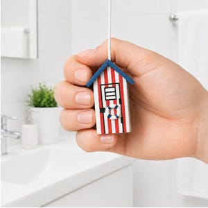 May include: A miniature beach hut-shaped light pull with red and white stripes, a blue roof, and a small life preserver detail. The pull is suspended by a white cord, perfect for a bathroom or coastal-themed decor.