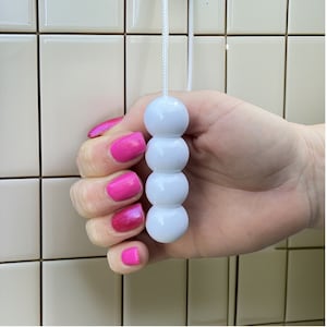 Puede incluir: Una cadena de tracción de luz blanca con cuentas. Las cuentas son redondas y lisas. La cadena está colgando de un techo.