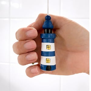 May include: A small lighthouse ornament with a blue and white striped design. The lighthouse has a dark blue top and base, with two small yellow windows. A white string is attached to the top.