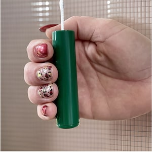 Puede incluir: Un cordón de tiro de plástico verde para persianas de ventana. El cordón se sostiene en una mano con esmalte de uñas de estampado de leopardo.