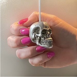 May include: A silver skull-shaped light pull with a detailed face and teeth.