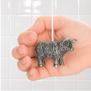 May include: A silver-toned metal Highland cow figurine attached to a white pull cord. The cow features detailed, textured fur, prominent horns, and four legs. The figurine is designed as a decorative pull for a light switch or ceiling fan.