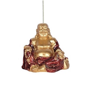 May include: A gold and red laughing Buddha figurine. The Buddha is sitting with his legs crossed and has a large belly. He is wearing a red robe with gold accents.